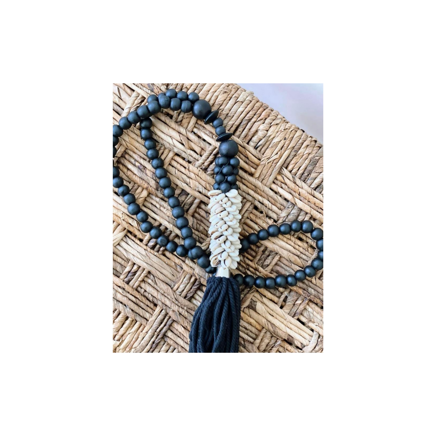 Black wood bead garland with beige shells and black cotton tassel on woven background